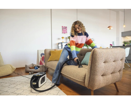 Femme nettoie un canapé avec un injecteur-extracteur dans un salon.