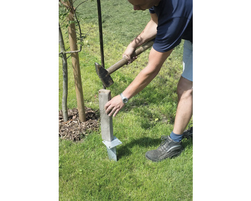 Eine Person schlägt einen Holzpfosten mit einem Hammer in den Boden.