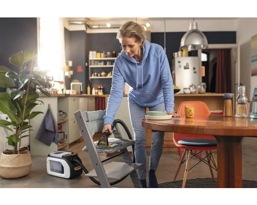 Eine Frau reinigt mit einem Waschsauger einen Kinderstuhl in einer Wohnung.