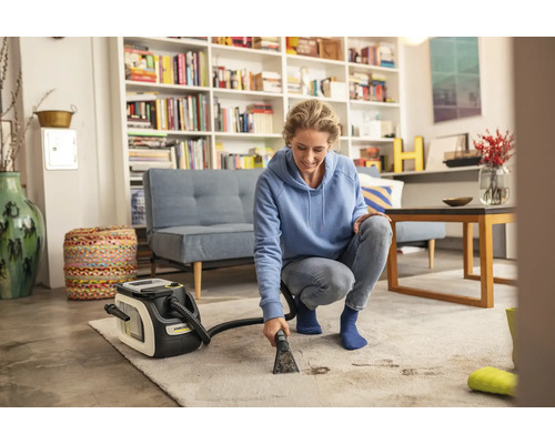 Frau reinigt Teppich mit einem Teppichreinigungsgerät der Marke Kärcher in einem Wohnzimmer.