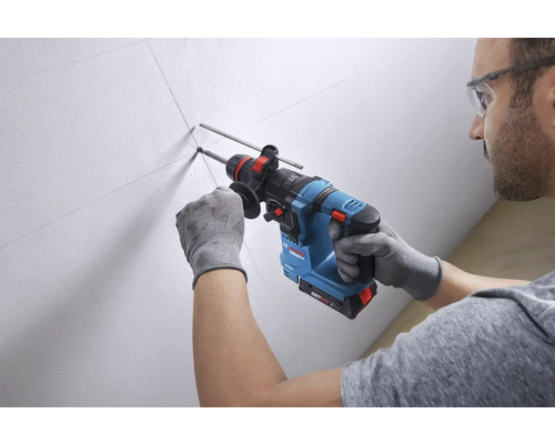 Mann bohrt mit einem Akku Bohrhammer ein Loch in eine Wand.