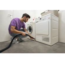 Un homme nettoie le sèche-linge avec un aspirateur dans une buanderie lumineuse.