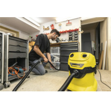 Un homme utilise un aspirateur Kärcher jaune dans un atelier pour nettoyer le sol.
