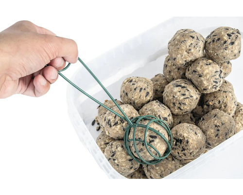 Hand nimmt einen Meisenknödel mit einem Greifer aus einem Behälter.