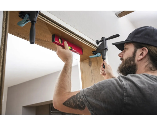 Handwerker montiert mit Wasserwaage und Schraubzwinge eine Türzarge.