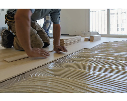 Pose d''un sol stratifié avec de la colle par un artisan dans une pièce lumineuse.