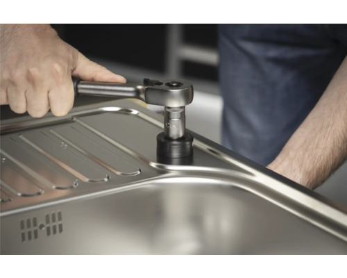 Une personne fixe un robinet à un évier avec une clé à douille.