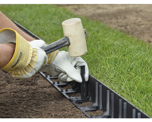 Une personne fixe une bordure de pelouse avec un maillet en caoutchouc.