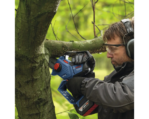 Un homme coupe une branche avec une tronçonneuse à batterie.