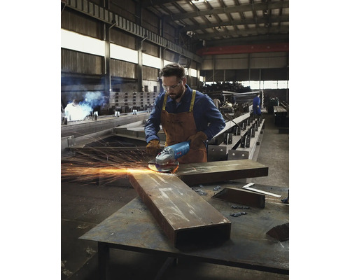 Un ouvrier utilise une meuleuse dans un atelier, des étincelles jaillissent.