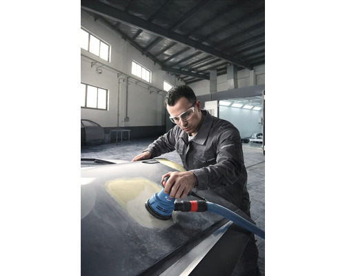 Un homme ponce une voiture avec une ponceuse excentrique dans un atelier.