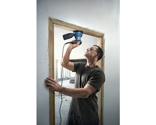 Un homme ponce un cadre de porte avec une ponceuse excentrique.