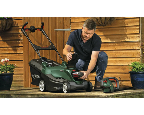 "Un homme insère une batterie dans une tondeuse à gazon sur une terrasse en bois 
