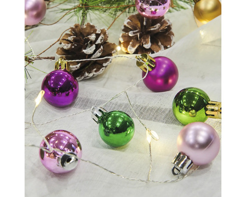 Dekorative Weihnachtskugeln mit Tannenzapfen und Lichterkette auf Stoff