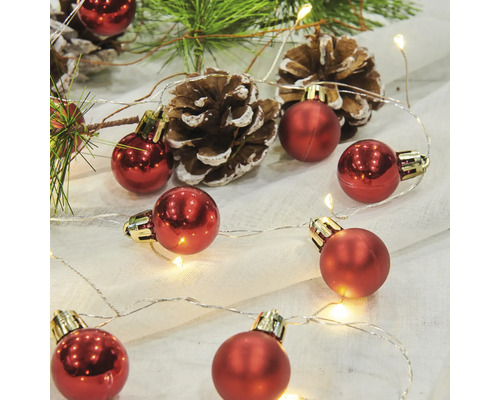 Dekorative Anordnung mit roten Weihnachtskugeln, Lichterkette, Tannenzweigen und Tannenzapfen.