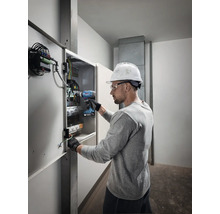 Elektriker arbeitet mit einem Akkubohrschrauber an einem Verteilerkasten.