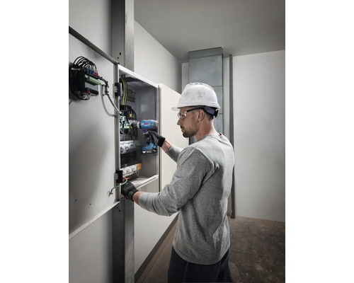 Elektriker arbeitet mit einem Akkubohrschrauber an einem Verteilerkasten.