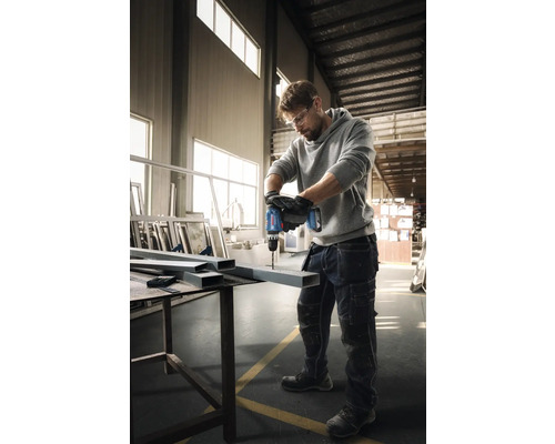 Ein Mann bohrt mit einem Akku-Bohrschrauber ein Loch in ein Metallprofil.