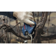 Une main gantée utilise un sécateur électrique Bosch pour tailler une branche.