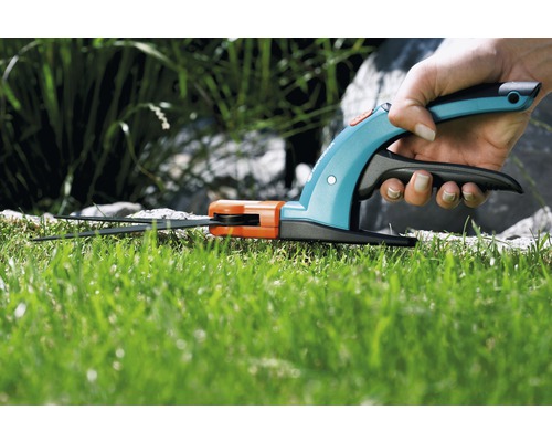 Hand hält eine Akku-Grasschere beim Grasschneiden