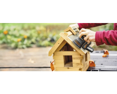 Eine Person schleift ein Vogelhaus mit einem Schwingschleifer der Marke WORX.