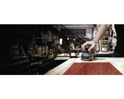 Ein Mann schleift Holz mit einem Exzenterschleifer in einer Werkstatt.