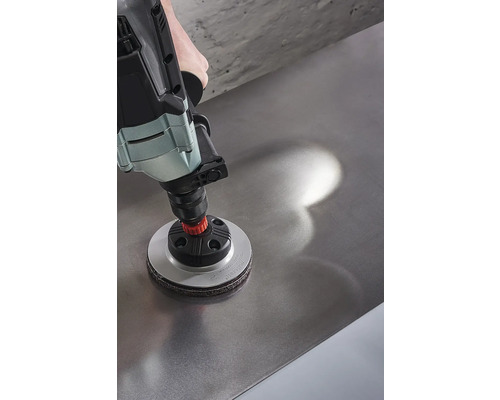 Une perceuse avec un accessoire de ponçage est utilisée sur une surface métallique.