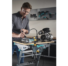 Mann mit Schutzbrille bearbeitet Metallteil auf einer Wolfcraft Werkbank mit einem Multifunktionswerkzeug.