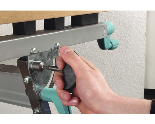 Eine Person befestigt eine Schraube mit einem Schraubendreher an einem Metallbettrahmen.