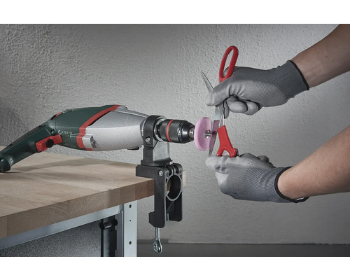 Une perceuse avec un accessoire de meulage monté est utilisée pour affûter des ciseaux.