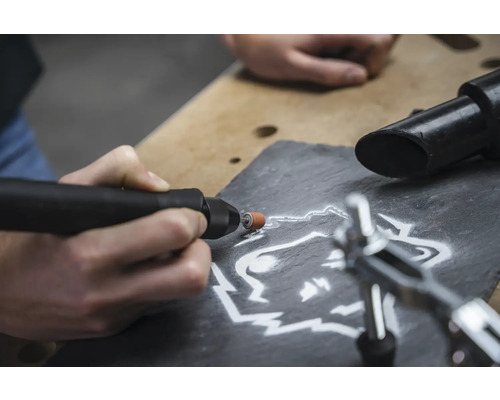 Gros plan d''une personne gravant un motif de loup dans une ardoise à l''aide d''un outil multifonction.