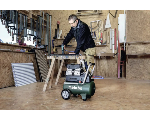 Un homme utilise un compresseur Metabo dans un atelier tout en travaillant sur une pièce.