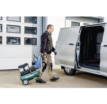 Artisan transportant un compresseur Metabo vers une camionnette.
