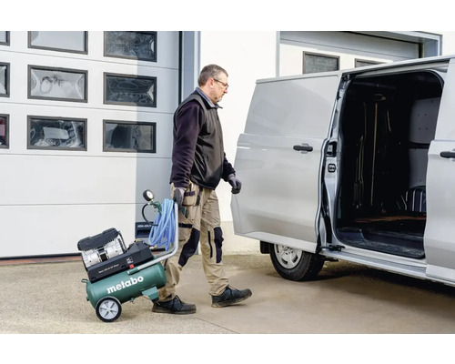 Artisan transportant un compresseur Metabo vers une camionnette.