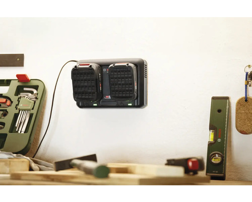 Akkuladegerät mit zwei Akkus an einer Wand in einer Werkstatt.