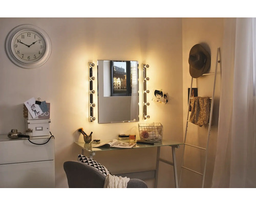 Helles Zimmer mit beleuchtetem Spiegel, Schreibtisch, Dekoration und Uhr an der Wand.