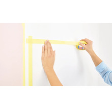 Eine Person klebt Malerkrepp an eine Wand.