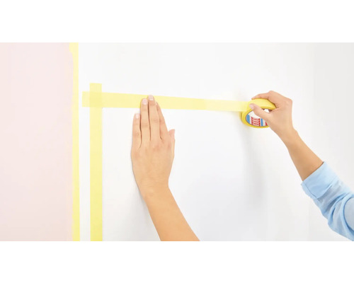 Une personne pose du ruban de masquage sur un mur.