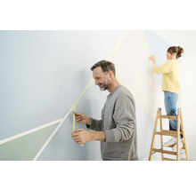 Zwei Personen gestalten eine Wand mit Klebeband für Malerarbeiten und geometrischen Formen.