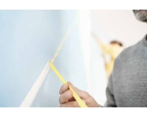 Un homme fixe du ruban de masquage sur un mur