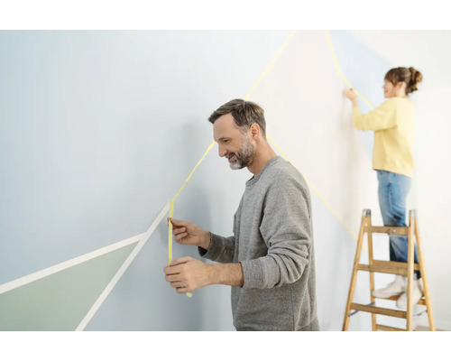 Zwei Personen gestalten eine Wand mit Malerkrepp für geometrische Formen.