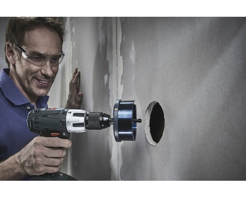 Un homme perce un trou dans un mur avec une scie cloche