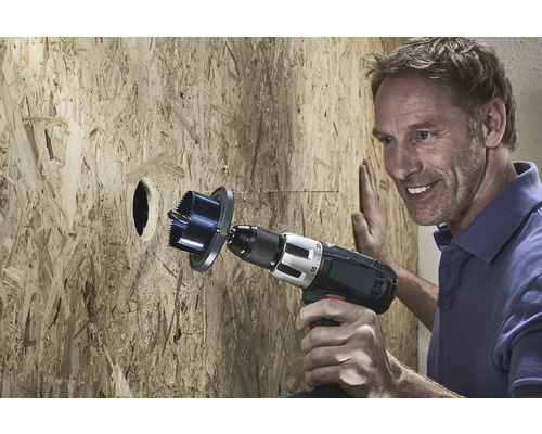 Un homme perce un trou dans une plaque de bois avec une scie trépan.