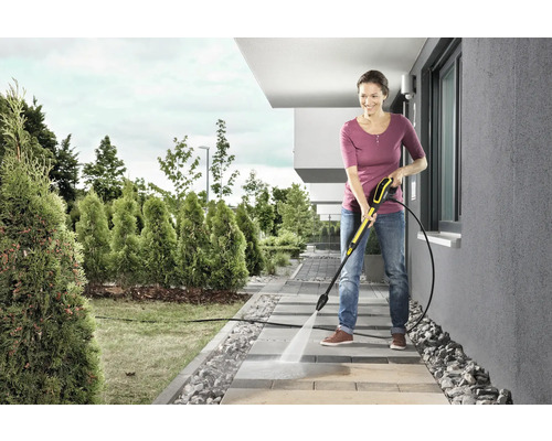 Une femme nettoie des dalles de trottoir avec un nettoyeur haute pression dans le jardin.