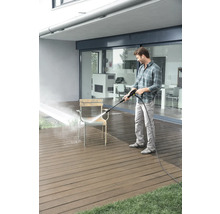Homme nettoie une chaise avec un nettoyeur haute pression sur une terrasse.