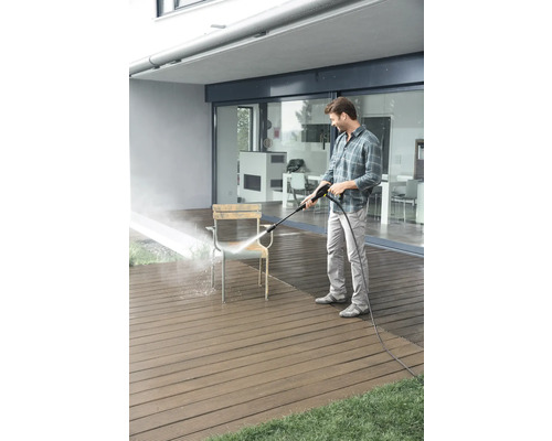 Homme nettoie une chaise avec un nettoyeur haute pression sur une terrasse.