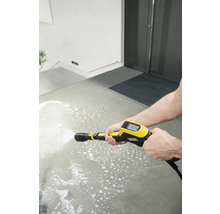 Une personne nettoie une surface en béton avec un nettoyeur haute pression jaune.