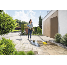 Une femme nettoie des pavés avec un nettoyeur de terrasse Kärcher devant une maison.