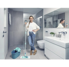 Helles Badezimmer mit Frau, die einen Mopp und einen Eimer hält, neben einem Waschbeckenunterschrank, einer Toilette und einer Dusche.