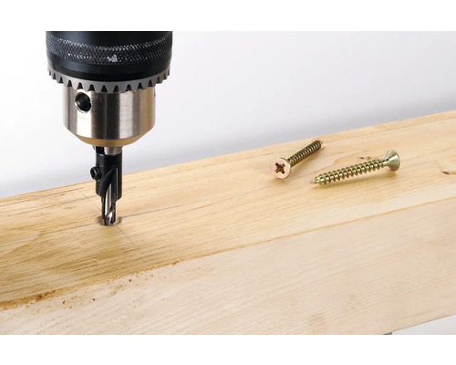 Bohrmaschine mit Senker bohrt in ein Holzbrett, daneben liegen zwei Schrauben